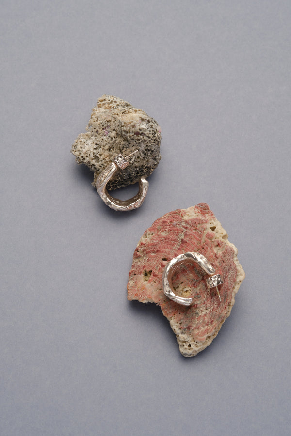 Layered Earth Hoop Earrings in silver: hoop earrings arranged on rough stone fragments.