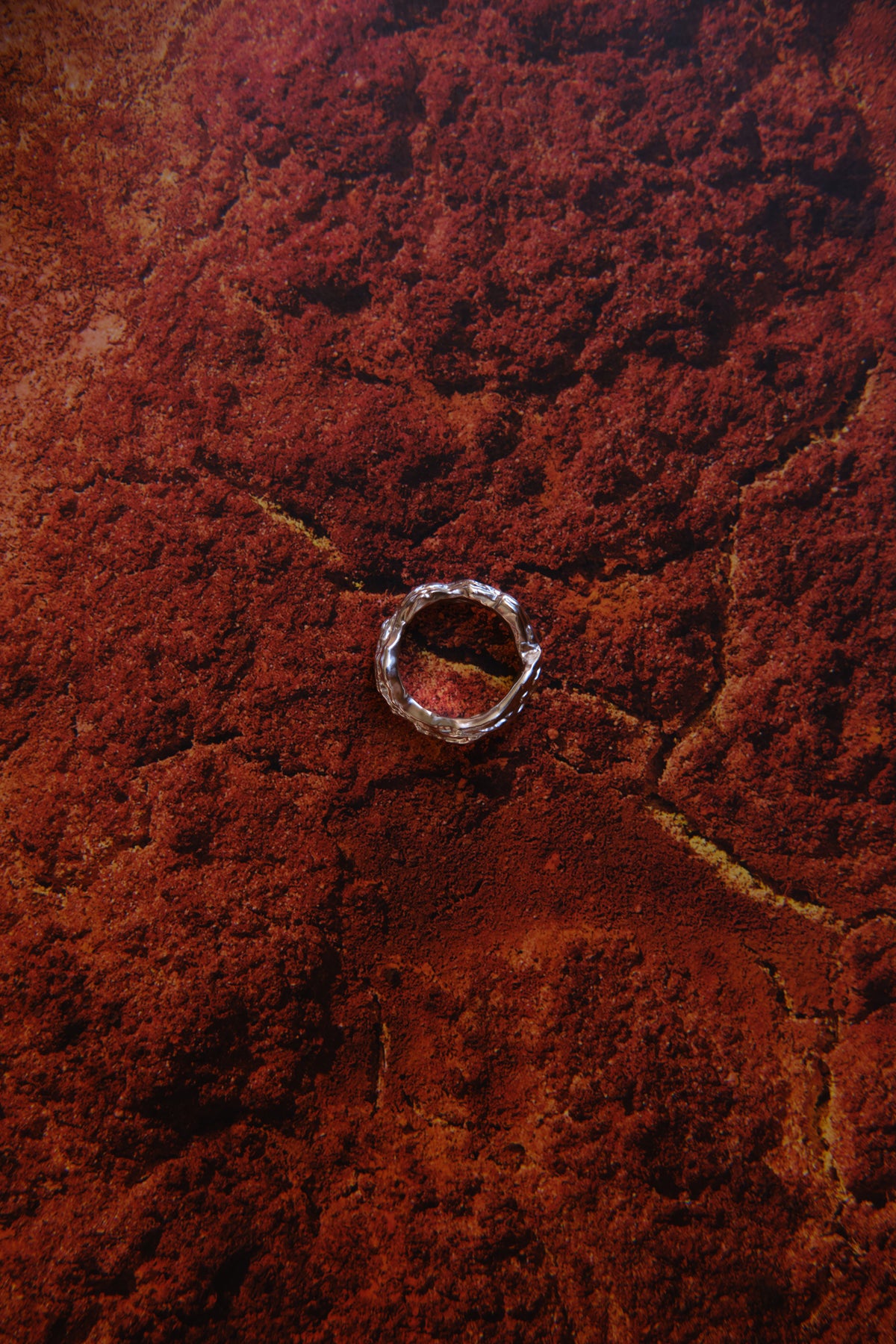 Layered Earth Ring in silver: ring styled on a textured red surface.