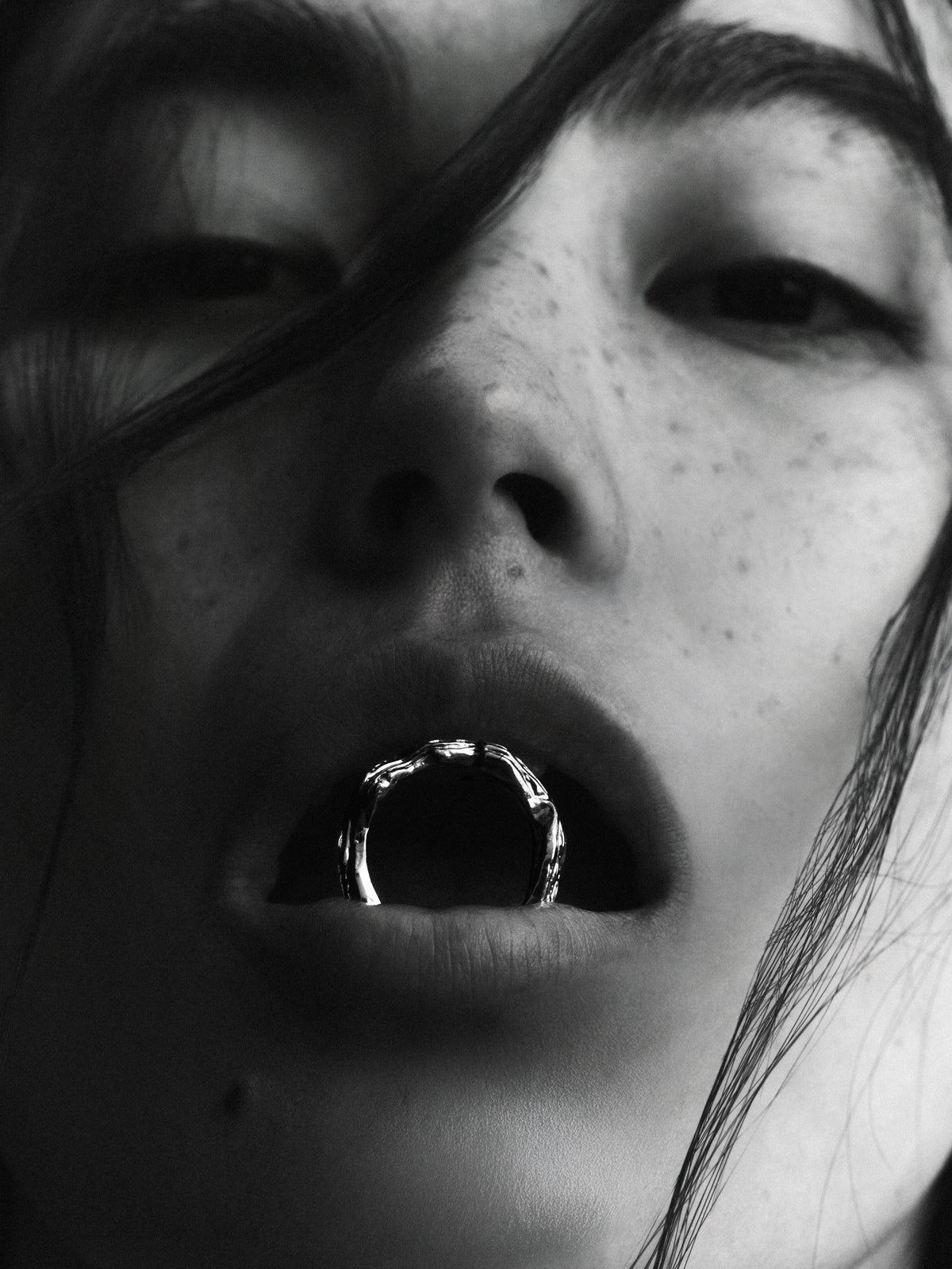 Layered Earth Ring in silver: black-and-white close-up of a model holding a textured ring at the lips.