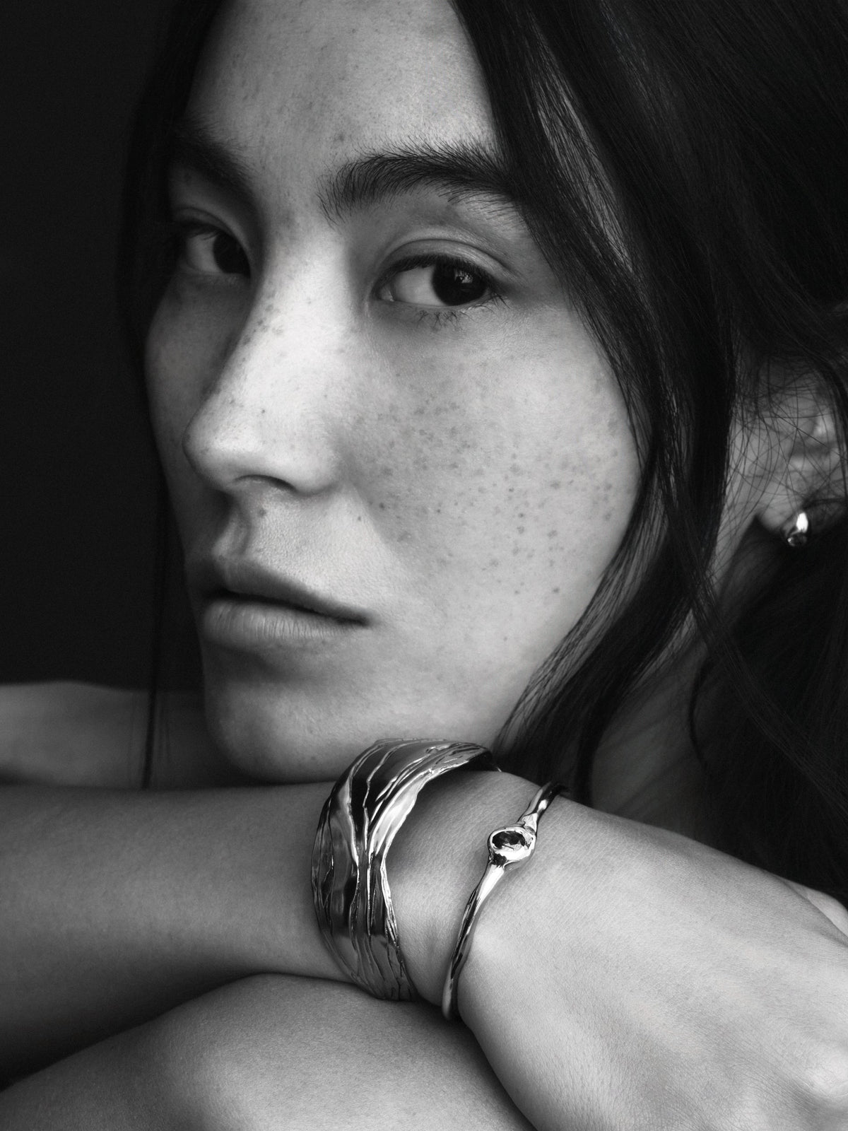 Layered Earth Statement Cuff in silver: black-and-white portrait of a model resting her face near a wrist wearing wide cuffs.