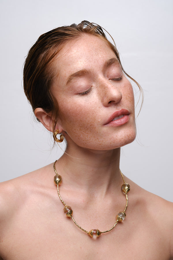 Close-up portrait of woman wearing sculptural gold necklace with organic pearl details