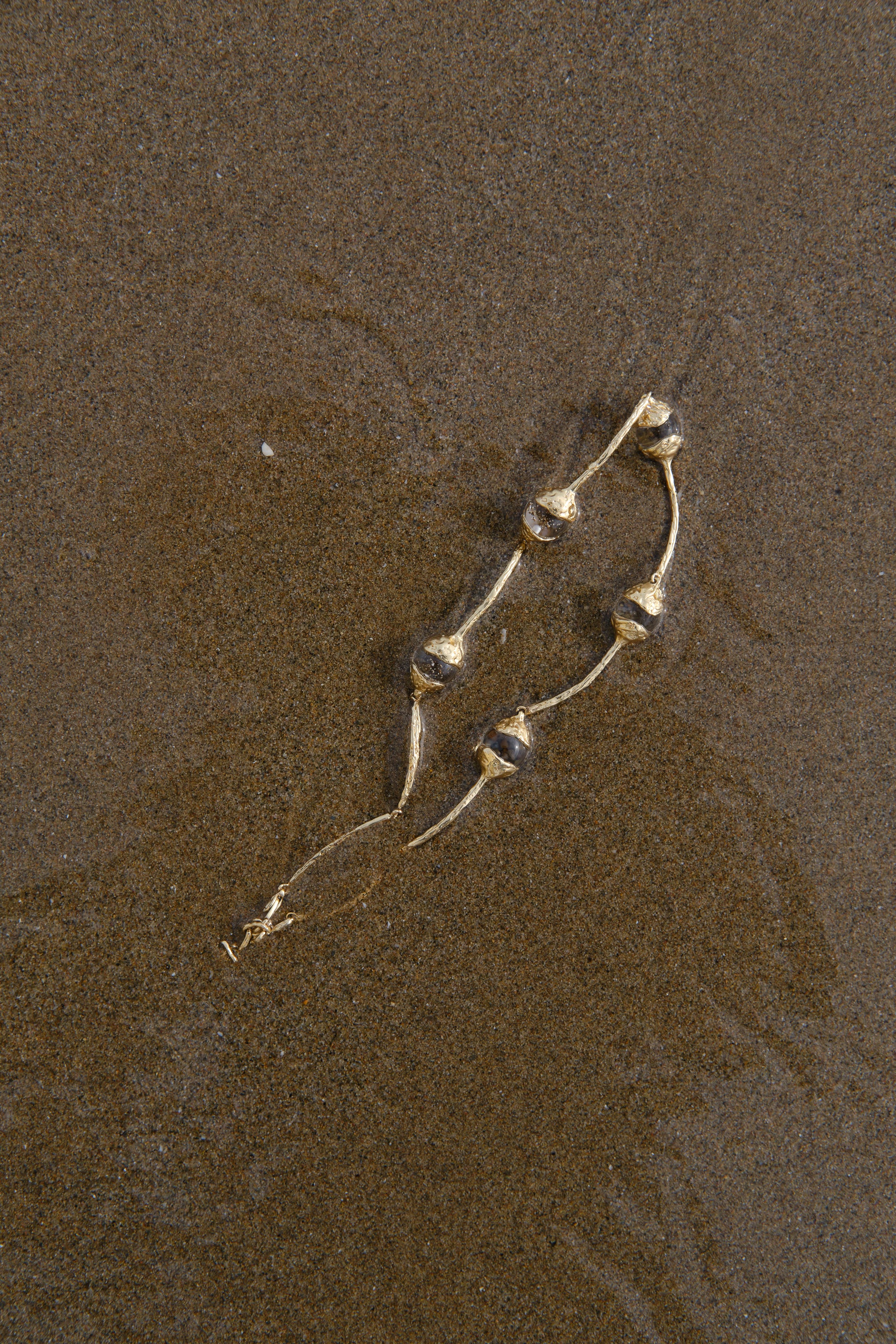 Sculptural gold necklace with organic pearl details styled on textured sand background