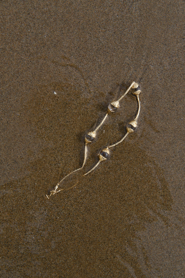 Sculptural gold necklace with organic pearl details styled on textured sand background