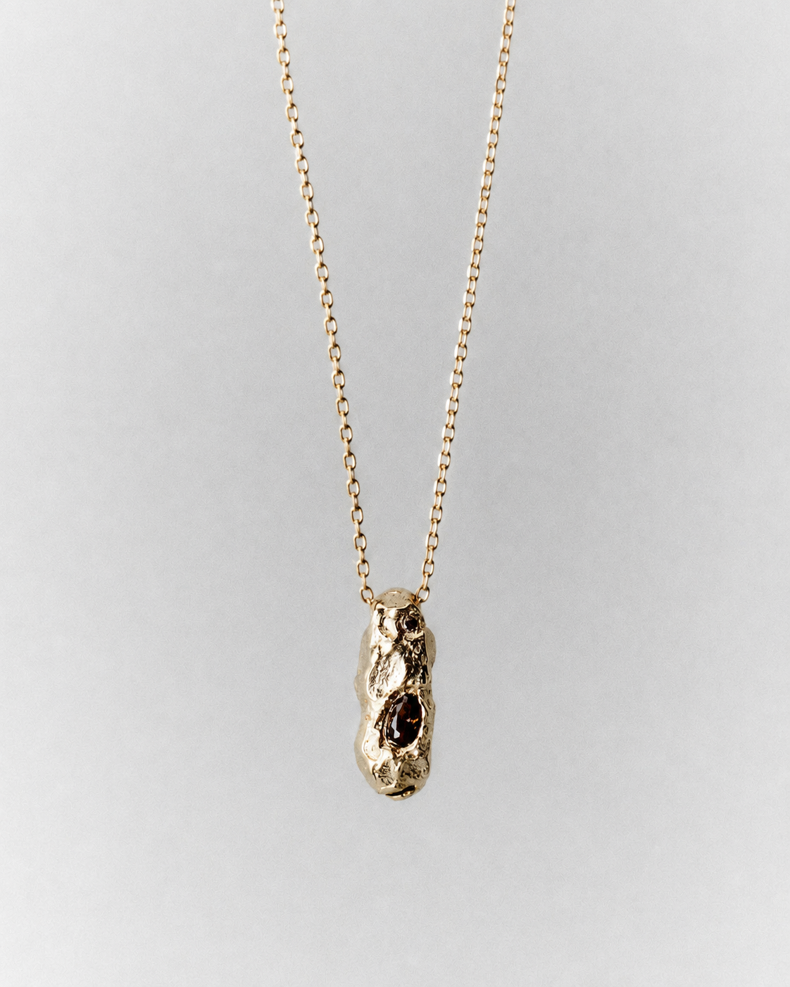 Sia Necklace in gold: fine necklace with a small sculptural pendant and dark inset stones.