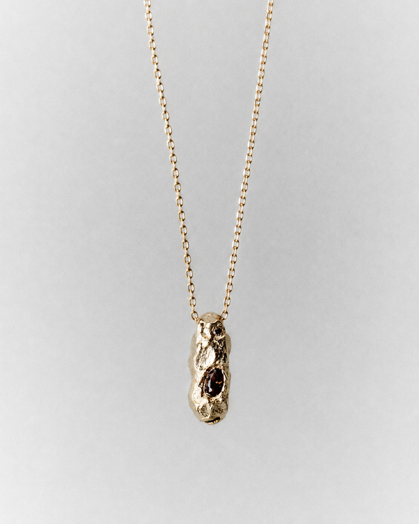 Sia Necklace in gold: fine necklace with a small sculptural pendant and dark inset stones.