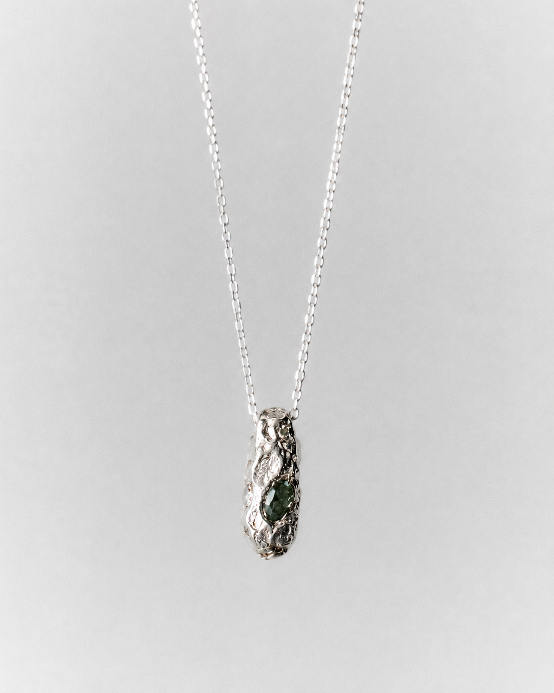 Sia Necklace in silver: fine necklace with a small sculptural pendant and green inset stone.