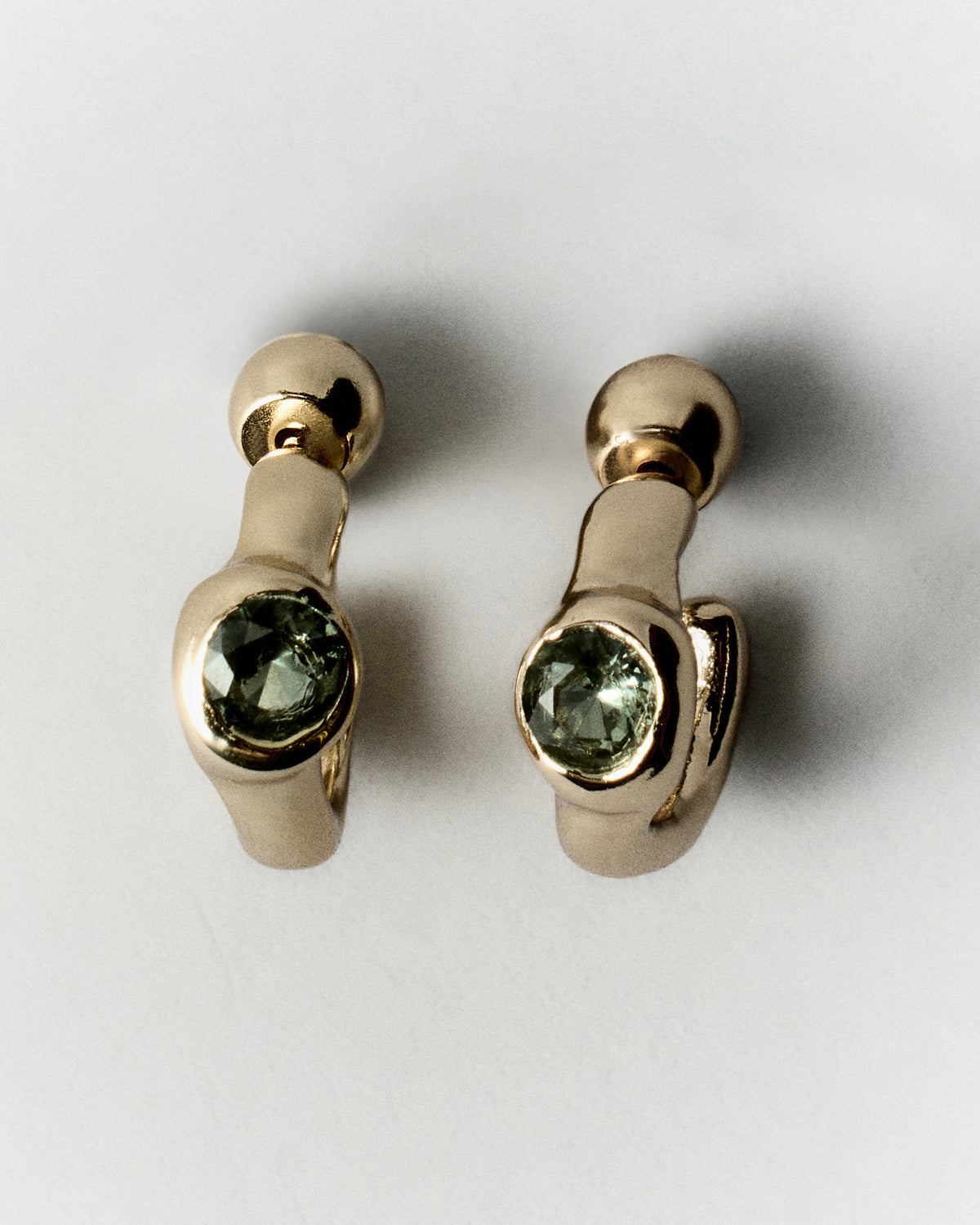 Tonka Mini Hoops in gold: pair of small sculptural hoops with green inset stones.