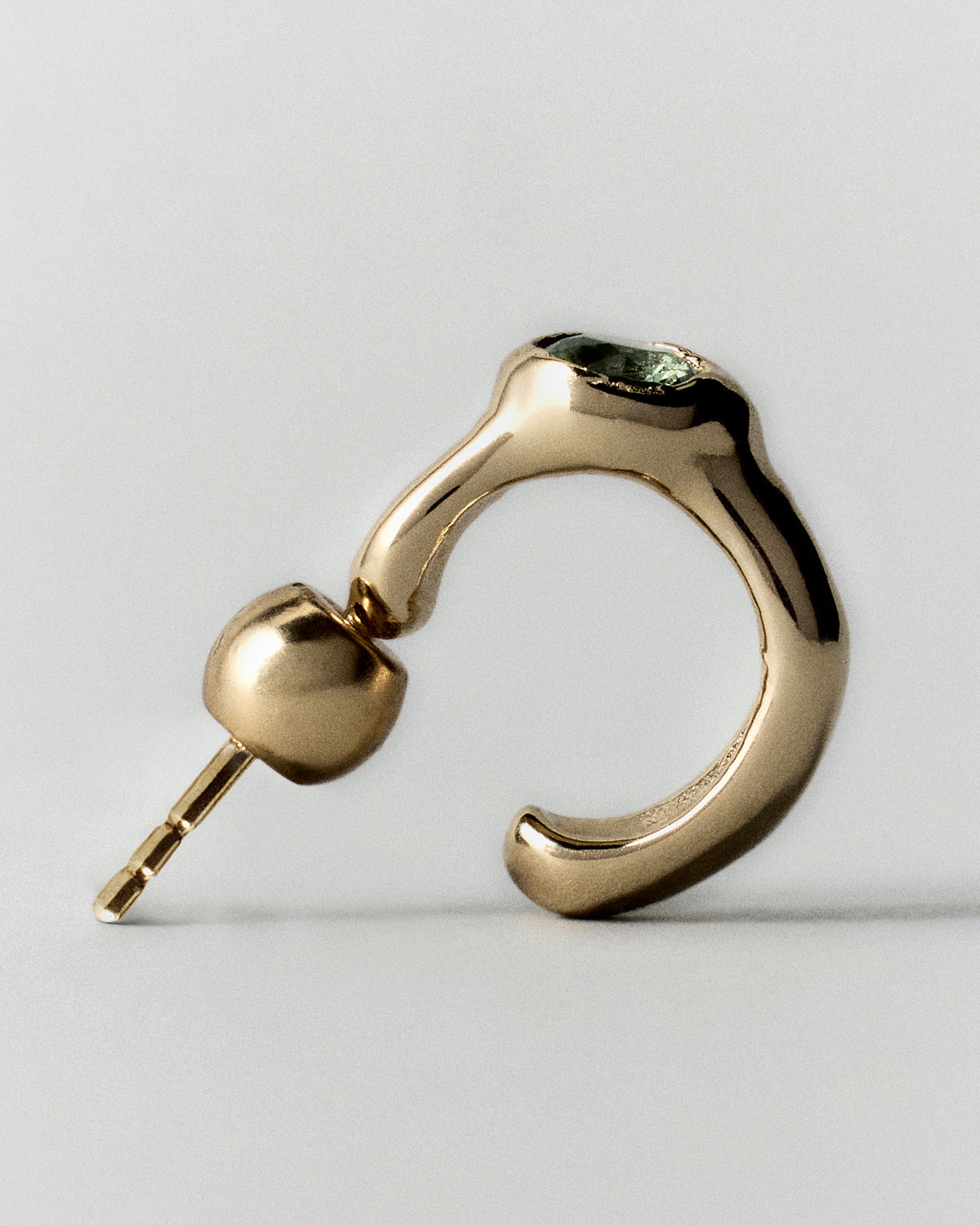 Tonka Mini Hoops in gold: side view of a single small hoop showing its green stone and post.