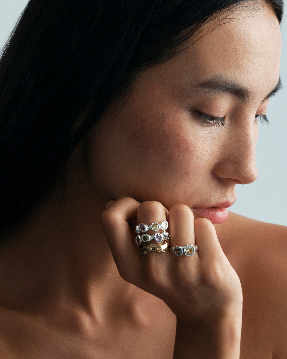 Tonka Ring in silver: portrait of a model resting her face on a hand wearing several stone-set rings.