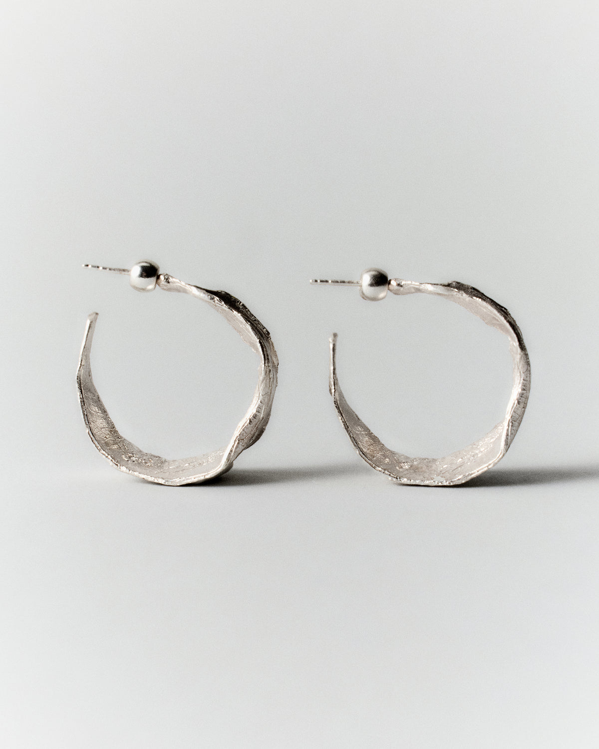 Vitalis II Hoops in silver: pair of broad open hoop earrings shown from the side.