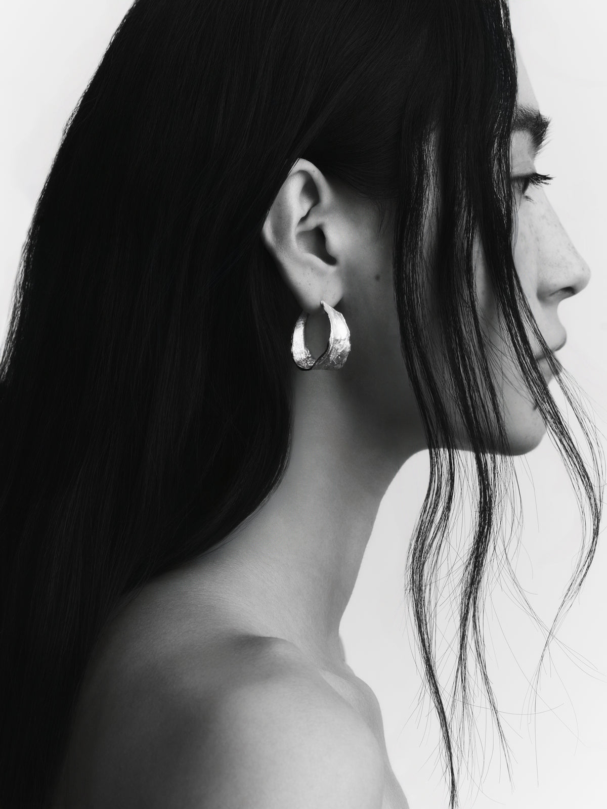 Vitalis II Hoops in silver: black-and-white side portrait of a model wearing broad textured hoops.