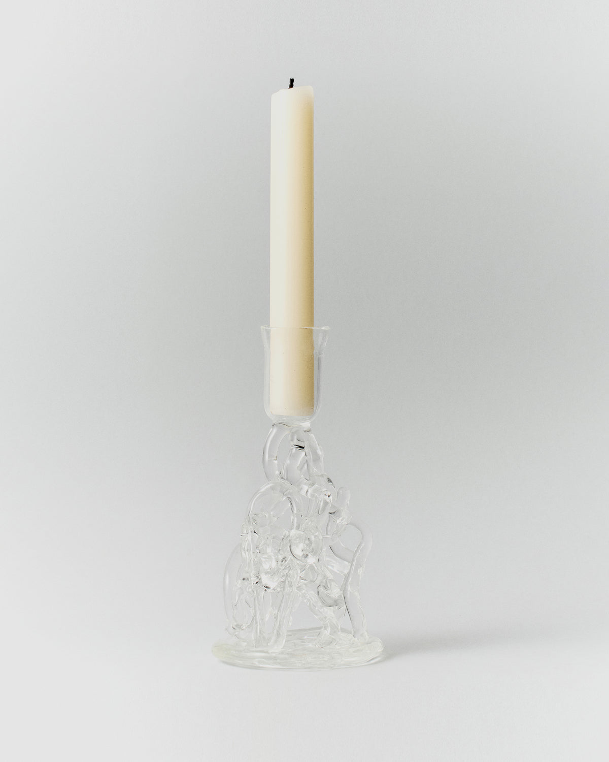 Watercousre Glass Candle Holder: clear sculptural glass candle holder with a lit taper candle.